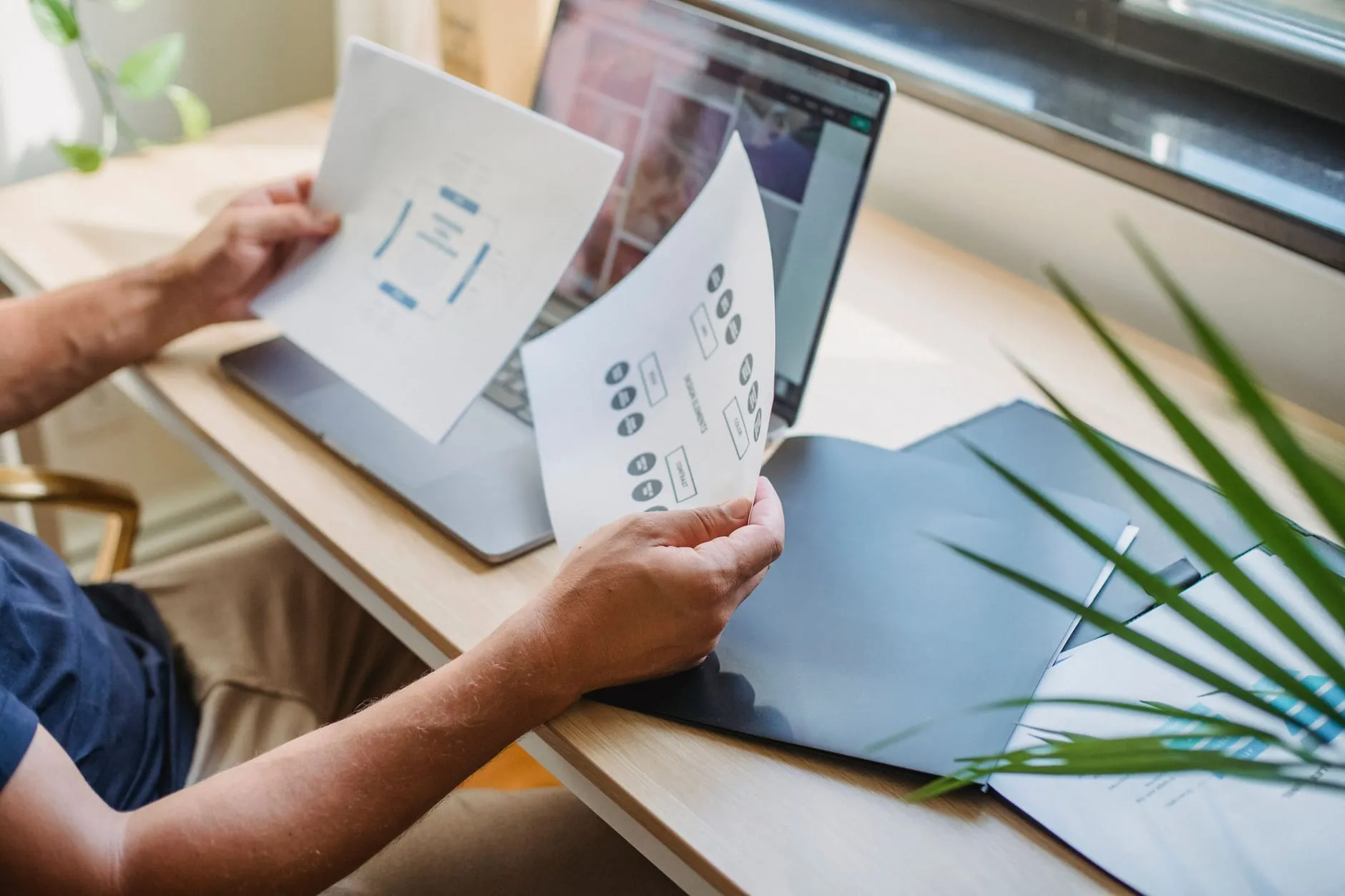 A designer comparing printed page layouts beside an open laptop, representing choosing the right website platform