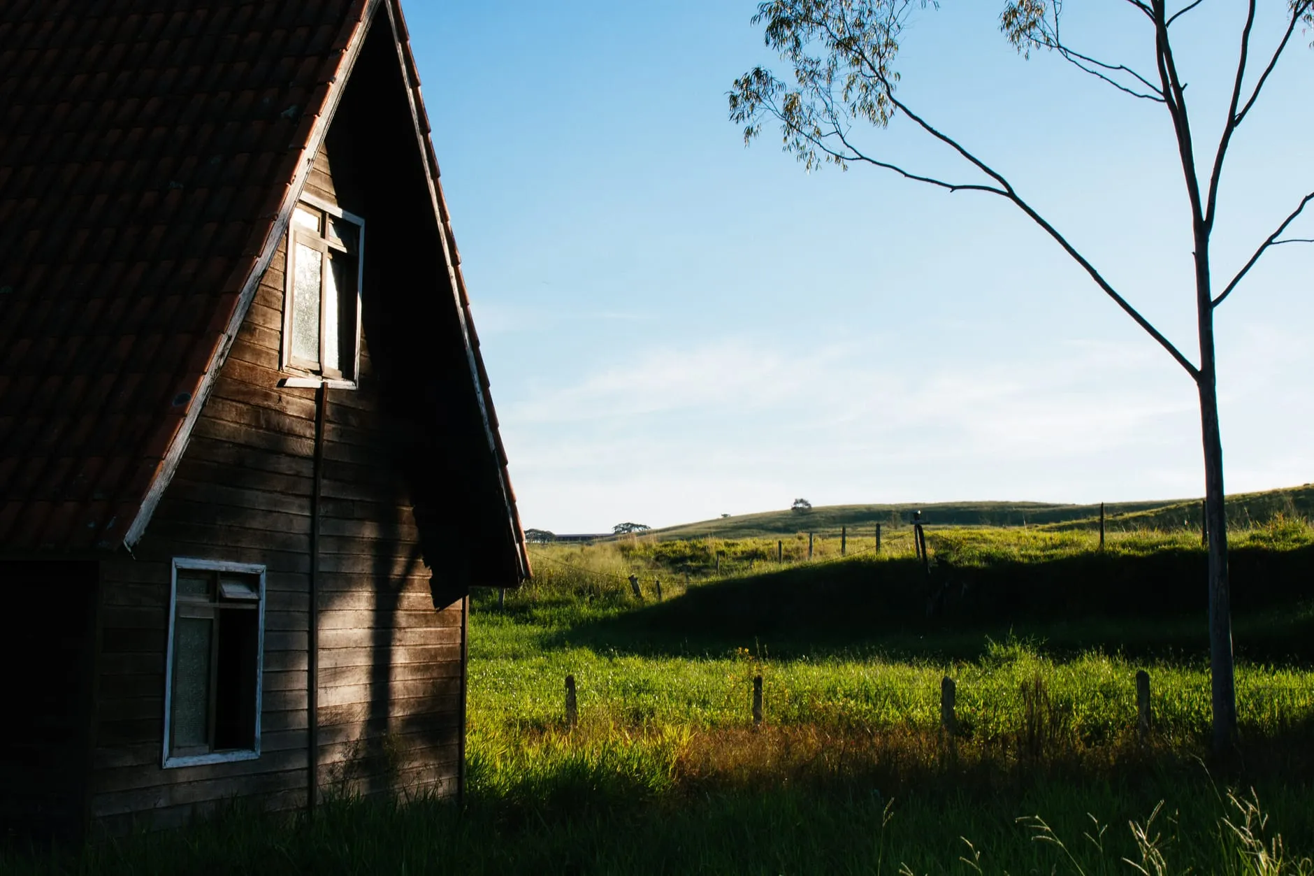 A timber cabin beside open grassland under a clear sky
