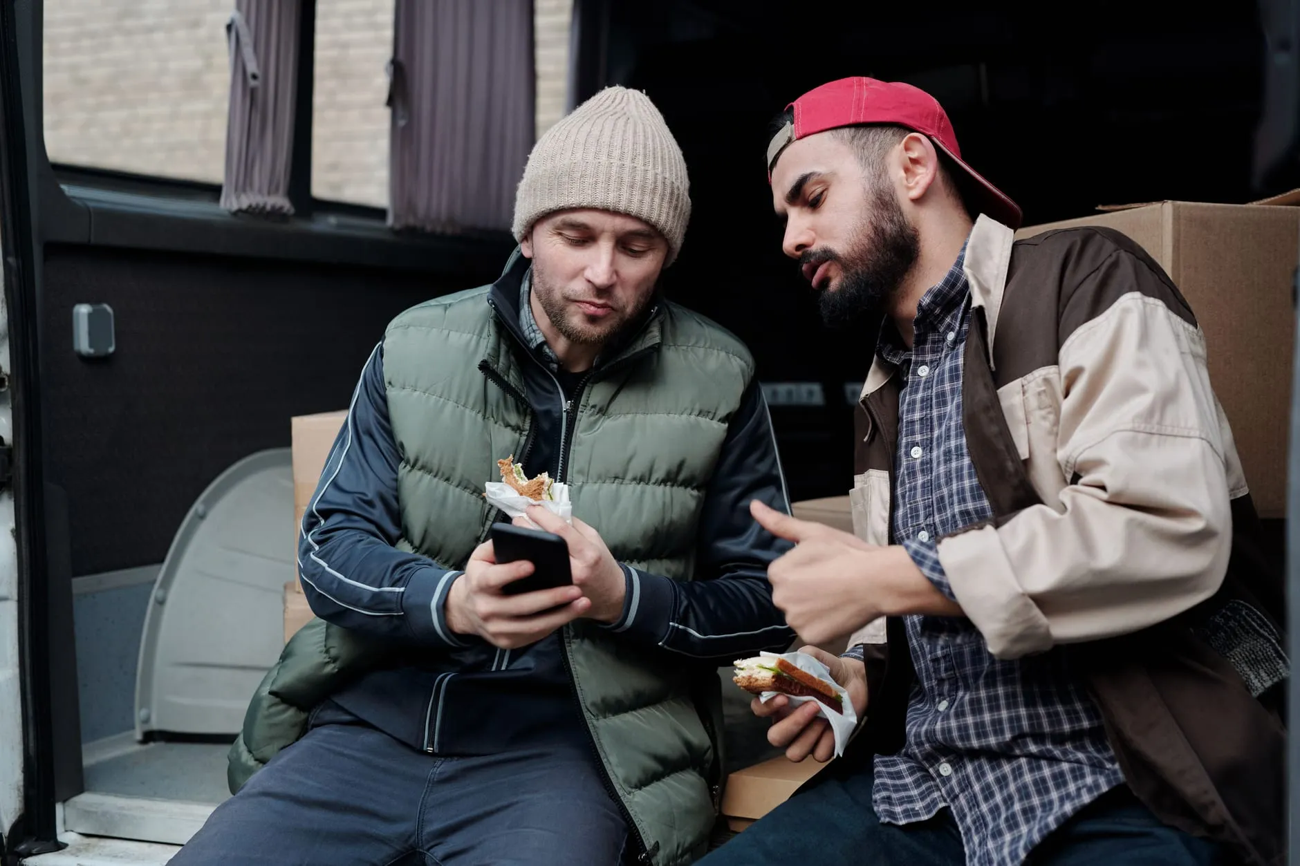Two tradespeople taking a break in their work van, one checking a phone