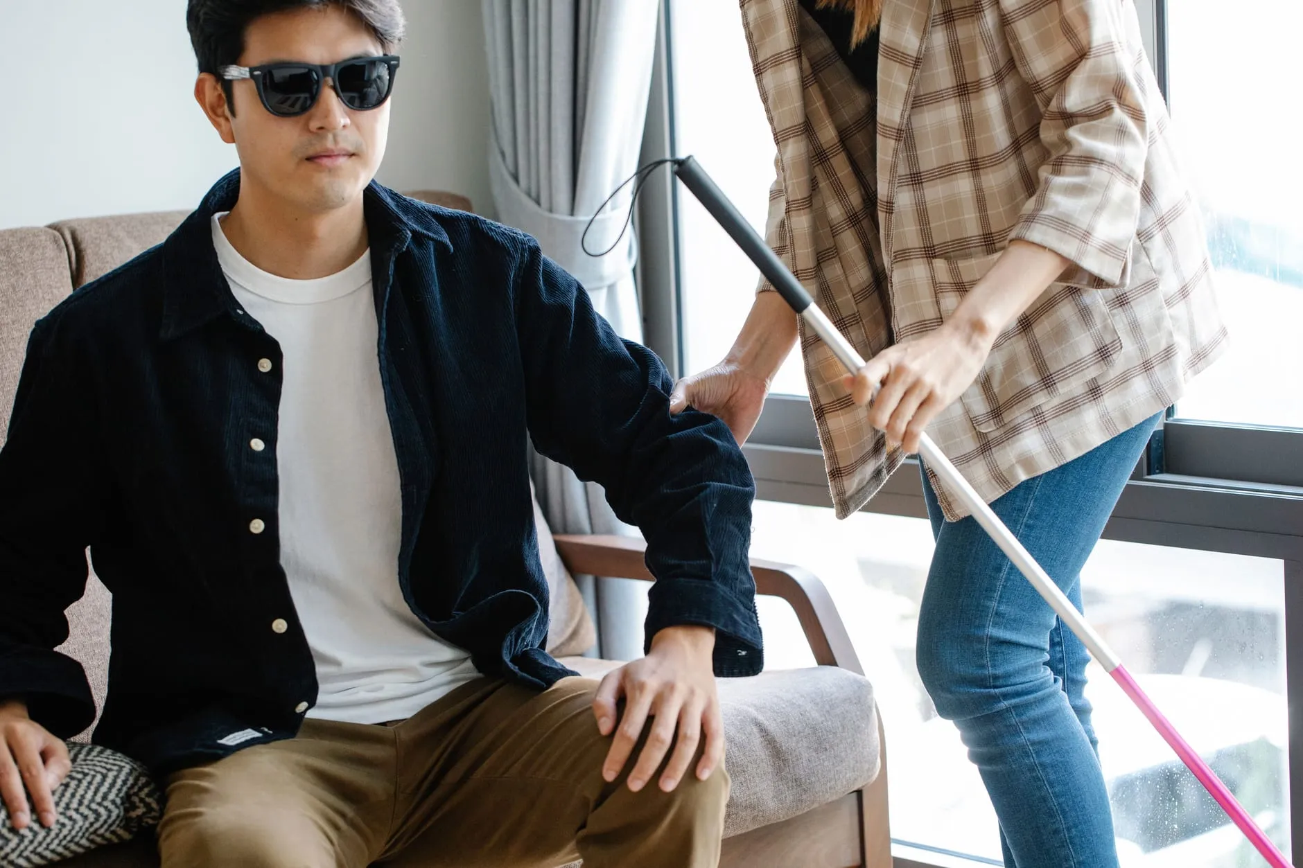 A support worker assisting a man with a white cane at home