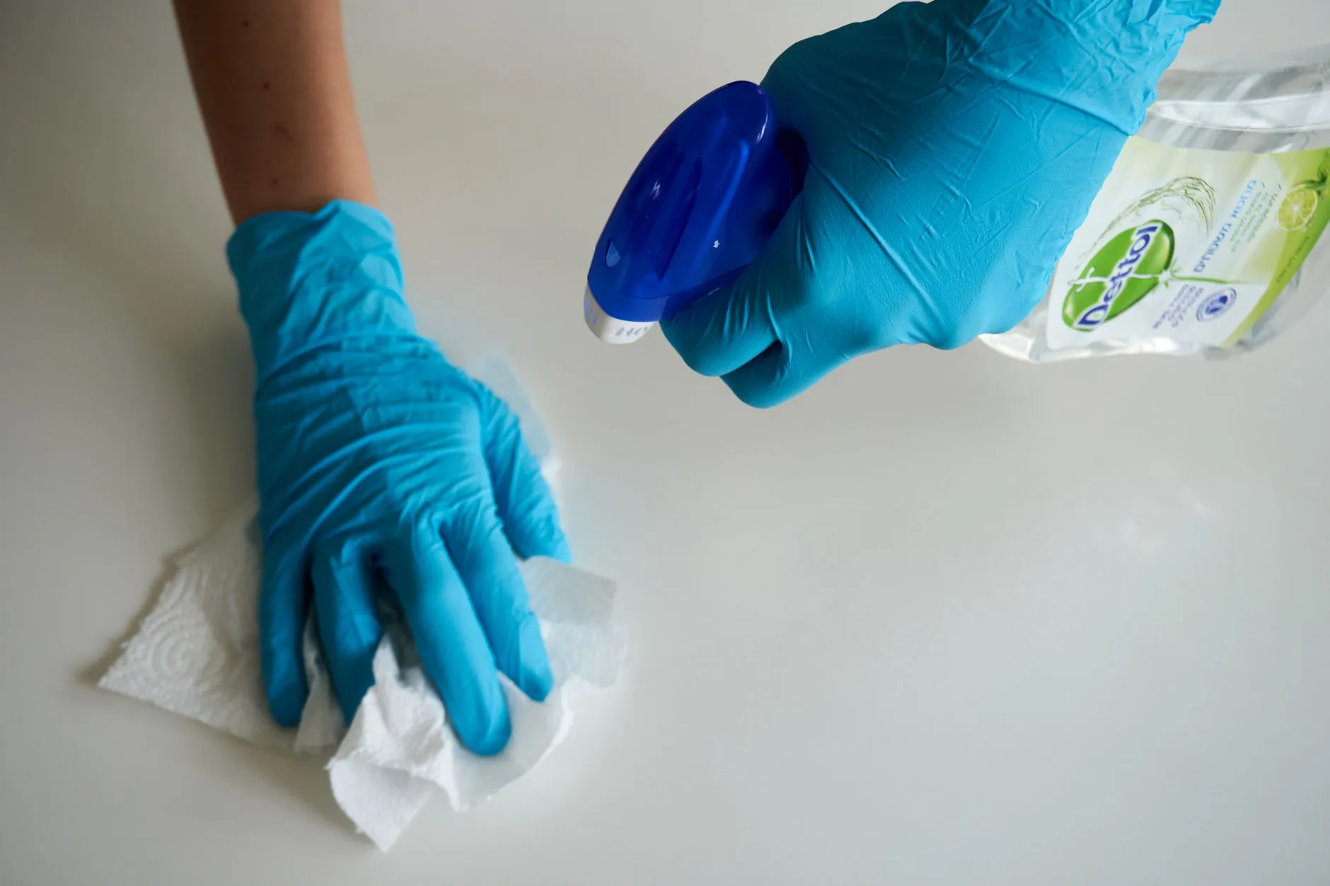 A cleaner wearing gloves wiping down and disinfecting a surface